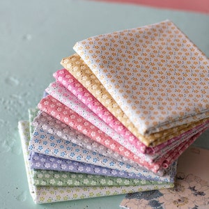 May include: A stack of eight fabric squares with a small floral pattern in various colors, including yellow, pink, green, and blue. The fabric squares are arranged in a graduated color scheme, with the lightest color on top and the darkest color on the bottom.