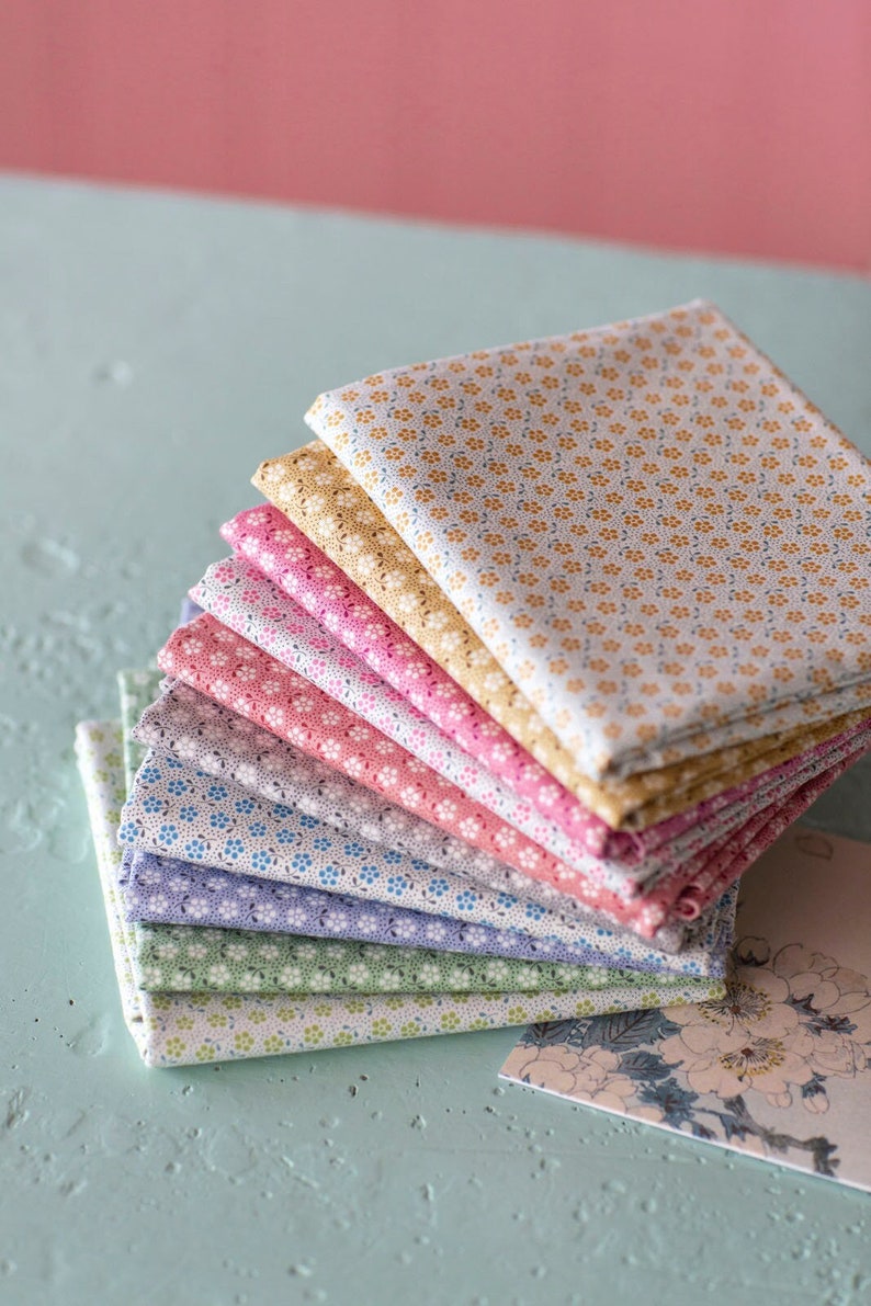 May include: A stack of eight fabric squares with a small floral pattern in various colors, including white, yellow, pink, red, blue, and green. The fabric squares are arranged in a fan shape.