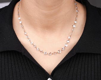 May include: A delicate rose gold chain necklace featuring a series of evenly spaced, round, clear faceted stones. The necklace rests against the neck, showcasing a minimalist design with a thin metallic link structure connecting each individual stone.