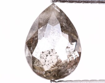 Puede incluir: Un diamante facetado en forma de pera, sujeto por unas pinzas metálicas. El diamante es de color gris y claro con inclusiones oscuras. La gema está tallada con múltiples facetas para reflejar la luz. Es una piedra preciosa.