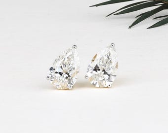 Op de afbeelding: Een paar peervormige diamanten oorstekers. Elke oorbel heeft een grote, heldere, facetgeslepen diamant gezet in een zilveren of witgouden prong setting. De oorbellen worden gepresenteerd op een witte ondergrond met een takje groen.