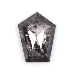 May include: A shield-cut, salt and pepper diamond with a unique shape. The gemstone features a mix of gray and black inclusions, creating a speckled appearance. The diamond's facets reflect light, showcasing its brilliance. The overall shape is a modified pentagon.