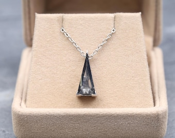 May include: A silver necklace with a triangular, dark gray pendant. The pendant is suspended from a delicate chain and is displayed inside a beige jewelry box. The necklace is a minimalist design.
