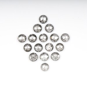 Może przedstawiać: Kolekcja okrągłych, szarych diamentów ułożonych w kształt rombu na białym tle. Każdy diament ma fasetowaną powierzchnię, odbijającą światło. Diamenty różnią się nieznacznie odcieniem, tworząc subtelną teksturę wizualną.