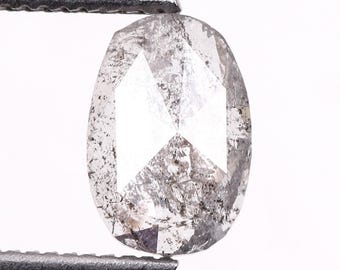 May include: A clear, oval-shaped diamond with gray inclusions, held by metal tweezers. The diamond's facets reflect light, showcasing its cut and clarity. The gemstone is set against a white background.