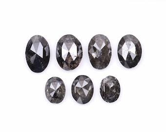 Pode incluir: Sete diamantes ovais, facetados, cinza escuro, estão dispostos sobre uma superfície branca. Os diamantes têm uma aparência salpicada e refletem a luz, mostrando seu corte e clareza. As pedras preciosas variam ligeiramente de tamanho.