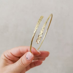 May include: A gold hammered metal bangle bracelet with a simple, open design.