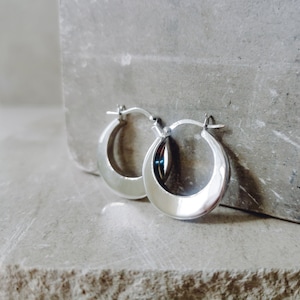 May include: A pair of silver hoop earrings with a smooth, rounded finish. The earrings are simple and elegant.