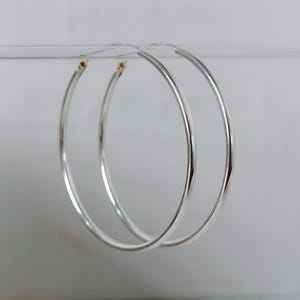 Peut inclure: Une paire de créoles en argent poli au design circulaire et lisse. Les boucles d'oreilles présentent une structure en fil de métal fin et arrondi formant une boucle continue, mettant en valeur une finition métallique réfléchissante sur toute la surface.