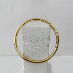 May include: A gold-colored bangle bracelet. The circular bracelet is displayed against a white, textured background. The bangle is a simple, elegant design, suitable for everyday wear.