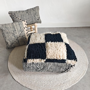 May include: A collection of decorative pillows and a floor cushion. The pillows have a black and white striped pattern with decorative stitching. The floor cushion has a checkerboard design in black and cream. The items are on a round, woven rug.