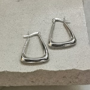 May include: A pair of silver triangle hoop earrings. The earrings are simple and modern in design.