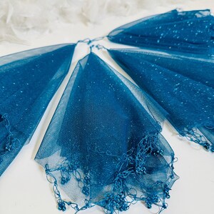 Puede incluir: Cuatro piezas de tela de tul azul turquesa con un borde de cuentas. La tela es transparente y tiene un acabado brillante.