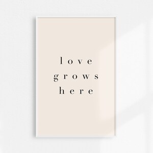May include: A white framed print with a beige background and the text "love grows here" in black.
