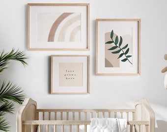 May include: Three framed prints on a white wall above a wooden crib. The prints feature abstract designs in neutral colors with a green leaf and the text "love grows here".