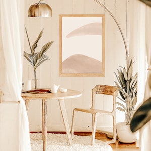 May include: A white round rug with a wooden table and chair in a room with white walls and a framed abstract painting with pink and white colors.