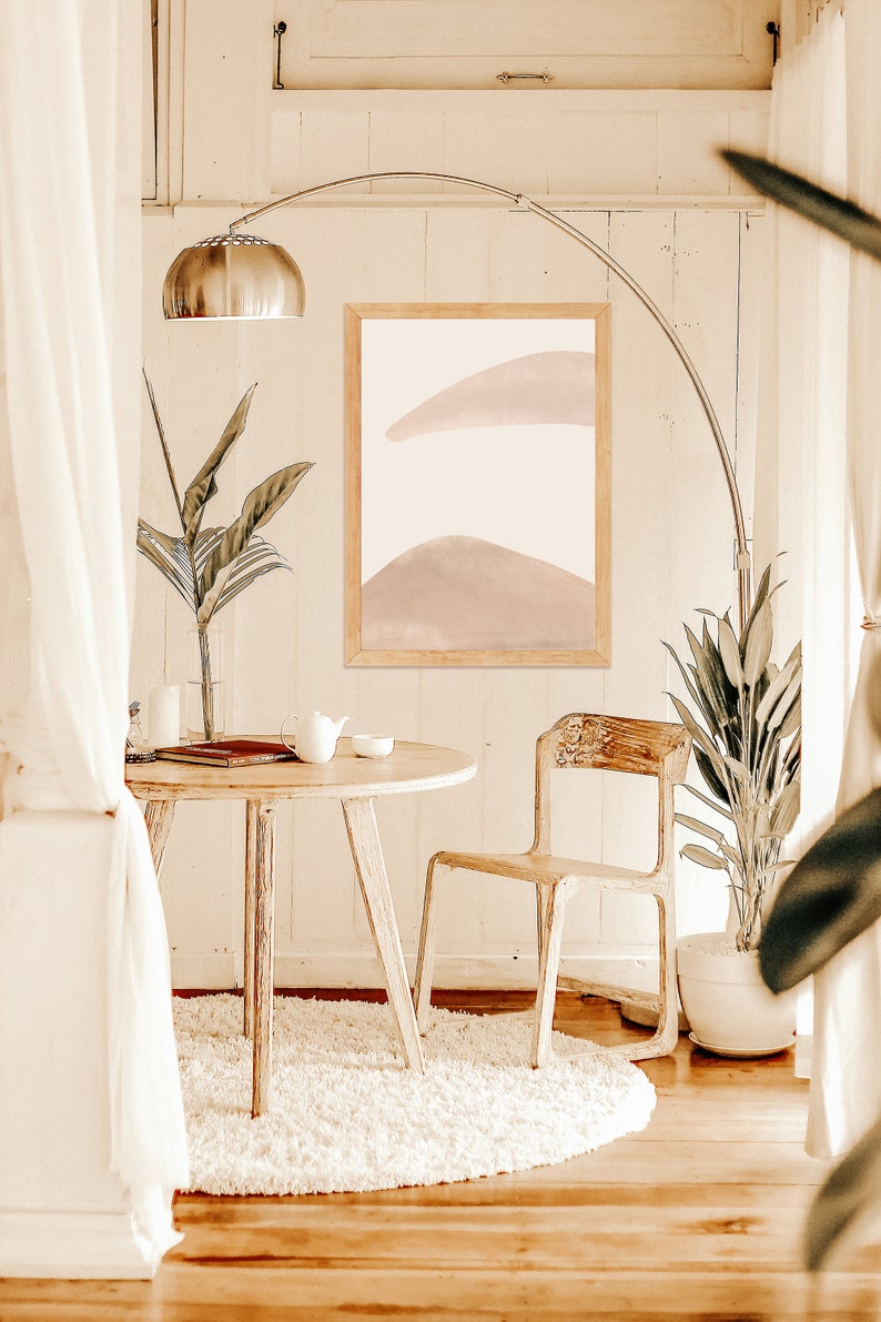 May include: A white round rug with a wooden table and chair in a room with white walls and a framed abstract painting with pink and white colors.
