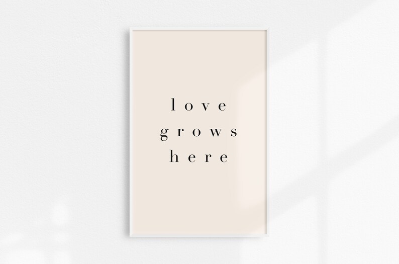 May include: A white framed print with a beige background and the text "love grows here" in black.