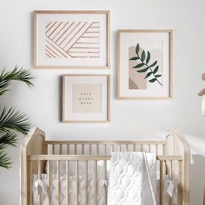 May include: A white crib with a white quilted blanket and three framed prints on the wall. The prints feature abstract designs in brown and beige, a green leaf, and the text "love grows here".