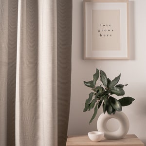 May include: A light brown wooden nightstand with a woven rattan drawer and a white ceramic vase with a ring design. The vase holds a leafy green plant. A framed print with the text "love grows here" hangs on the wall behind the nightstand.