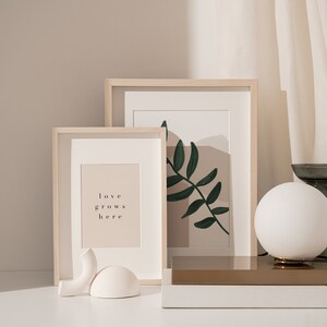 May include: Two framed prints on a white surface with a white globe lamp and a gray vase. The print on the left says "love grows here". The print on the right has a green leaf design.