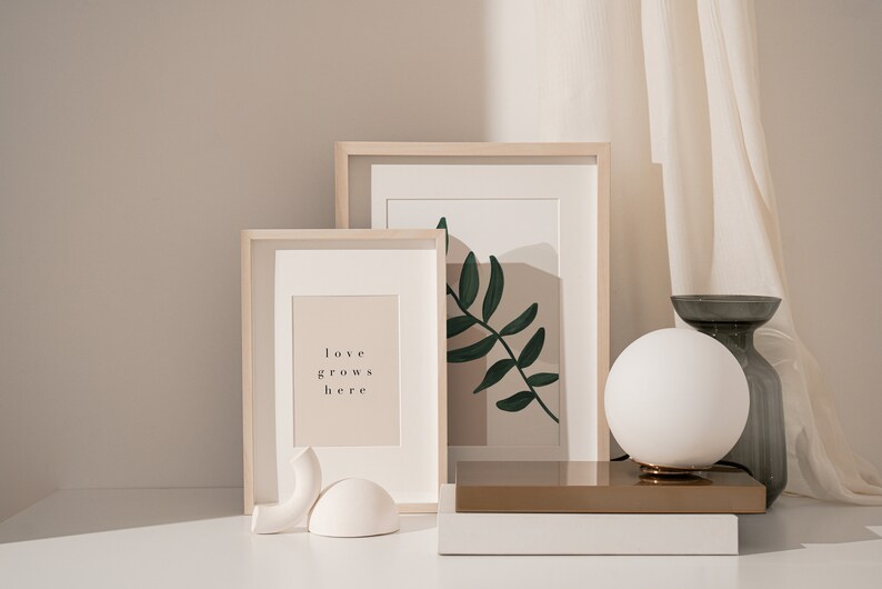 May include: Two framed prints on a white surface with a white globe lamp and a gray vase. The print on the left says "love grows here". The print on the right has a green leaf design.