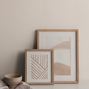 May include: Two framed abstract art prints with a minimalist aesthetic. The print on the left features brown lines on a white background. The print on the right features a light brown watercolor design on a white background.