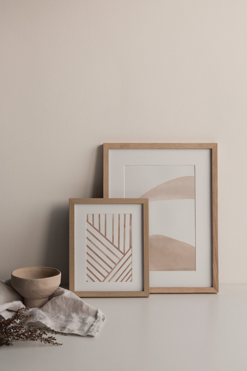 May include: Two framed abstract art prints with a minimalist aesthetic. The print on the left features brown lines on a white background. The print on the right features a light brown watercolor design on a white background.