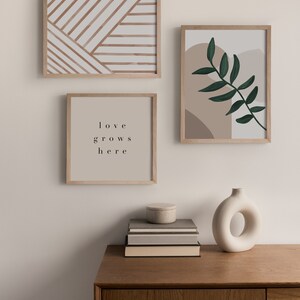May include: Three framed prints on a white wall above a wooden dresser. The prints feature abstract geometric patterns, a leafy branch, and the text "love grows here". A white ceramic vase sits on the dresser.