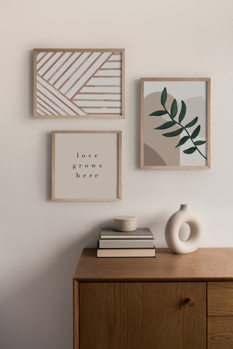 May include: Three framed prints on a white wall above a wooden dresser. The prints feature abstract geometric patterns, a leafy branch, and the text "love grows here". A white ceramic vase sits on the dresser.