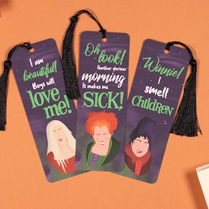 Op de afbeelding: Drie paarse bladwijzers met zwarte kwastjes met illustraties van de Sanderson-zussen uit de film Hocus Pocus. De tekst op de bladwijzers luidt: "Ik ben mooi! Jongens zullen van me houden!"  "Oh kijk! Nog een glorieuze ochtend. Het maakt me ziek!" en "Winnie! Ik ruik kinderen."