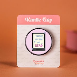 May include: A pink and black phone grip with the text "I'd rather stay home and read" on a white background. The grip is designed to look like a Kindle e-reader.
