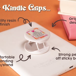 May include: White Kindle with a white and pink pop-up grip featuring the text "THIS KINDLE CONTAINS EXPLICIT CONTENT." The grip has a strong peel-off sticky back and a comfortable expanding grip/stand. The image also shows the text "Our Kindle Grips..." and "Paperback Addiction".
