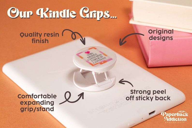 May include: White Kindle with a white and pink pop-up grip featuring the text "THIS KINDLE CONTAINS EXPLICIT CONTENT." The grip has a strong peel-off sticky back and a comfortable expanding grip/stand. The image also shows the text "Our Kindle Grips..." and "Paperback Addiction".