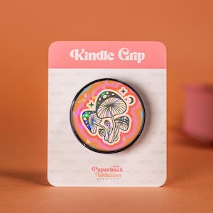 May include: A black phone grip with a holographic mushroom design on a pink and orange background. The grip says "Kindle Grip" and "Paperback Addiction" on the packaging.