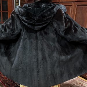 May include: A black hooded coat with a fur-trimmed hood and cuffs. The coat is open, showing the lining. The coat appears to be made of a soft, textured material, and is suitable for cold weather.