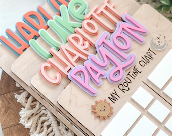 May include: A wooden personalized routine chart with a sun and moon design. The chart has blank spaces for writing in activities. The chart is personalized with the names "Hadrian", "Luke", "Charlotte", and "Payton" in colorful letters.