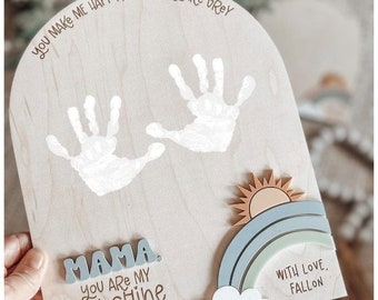 May include: A wooden sign with a handprint design and the text "You make me happy, when skies are grey. Mama, you are my sunshine, my only sunshine. With love, Fallon. Mothers Day 2024."