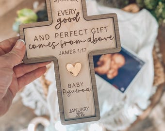 May include: A wooden cross-shaped plaque with the inscription "Every good and perfect gift comes from above, James 1:17." It includes a gold heart and the name "Baby Figueroa" with the date "January 2026."