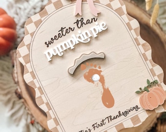 May include: Wooden sign with a light brown checkered border and a scalloped edge. The sign features the text "sweeter than pumpkin pie" and "Scottie's First Thanksgiving". A pink bow and a pumpkin graphic are also included.
