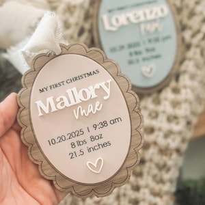 May include: A personalized Christmas ornament with the text "MY FIRST CHRISTMAS" and the name "Mallory Mae". The ornament includes birth details: 10.20.2025, 9:38 am, 8 lbs 8oz, and 21.5 inches. The ornament has a scalloped edge and a ribbon.
