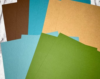 May include: A stack of different colored cardstock paper in shades of brown, blue, and green. The paper is arranged in a fan shape, with the green paper at the bottom and the brown paper at the top.