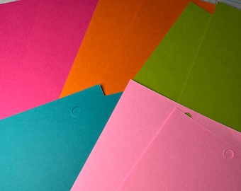 May include: Five sheets of cardstock in different colors: pink, orange, green, teal, and light pink. The sheets are stacked on top of each other and have a hole punched in the top right corner.