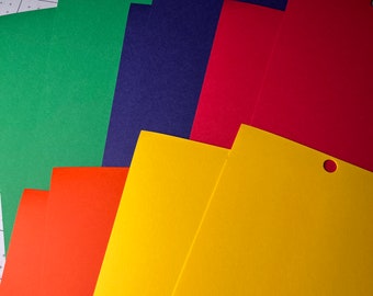 May include: A stack of colorful cardstock paper in green, blue, red, orange, and yellow. The paper is arranged in a fan shape with the top sheet having a hole punched in the upper right corner.