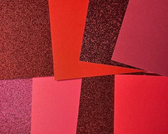 May include: A collection of red, pink, and burgundy textured paper sheets. The paper has a variety of textures, including glitter and a smooth finish.