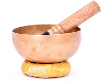 Può includere: Una ciotola cantate in ottone con un battitore in legno e un cuscino con motivo giallo. La ciotola è rotonda e ha una superficie liscia. Il battitore è lungo e ha un'estremità arrotondata. Il cuscino è piccolo e ha un motivo floreale.