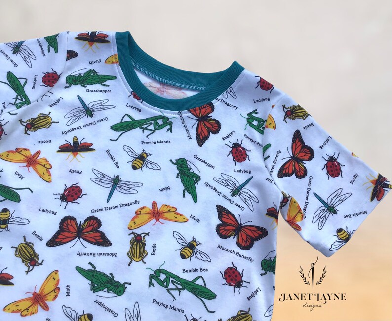 May include: White t-shirt with a colorful insect print. The shirt features a variety of insects, including butterflies, dragonflies, ladybugs, and praying mantises. The text on the shirt includes the names of the insects, such as "Monarch Butterfly", "Green Darner Dragonfly", and "Praying Mantis".