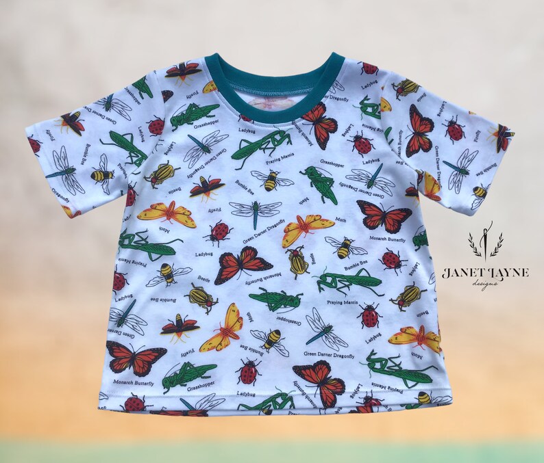 May include: White short-sleeved t-shirt with a colorful insect print. The print features butterflies, ladybugs, dragonflies, bees, and praying mantises. The shirt has a teal colored neckline.