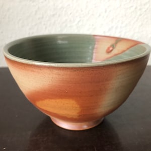 Könnte beinhalten: Eine Keramikschüssel mit einer hellgrünen Glasur innen und einer braunen Glasur außen. Die Schüssel hat eine leicht abgerundete Form und einen breiten Rand.