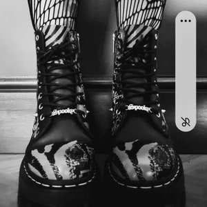 Puede incluir: Botas de plataforma de estampado de cebra en blanco y negro con hebillas plateadas que dicen "Spooky" en cada bota.